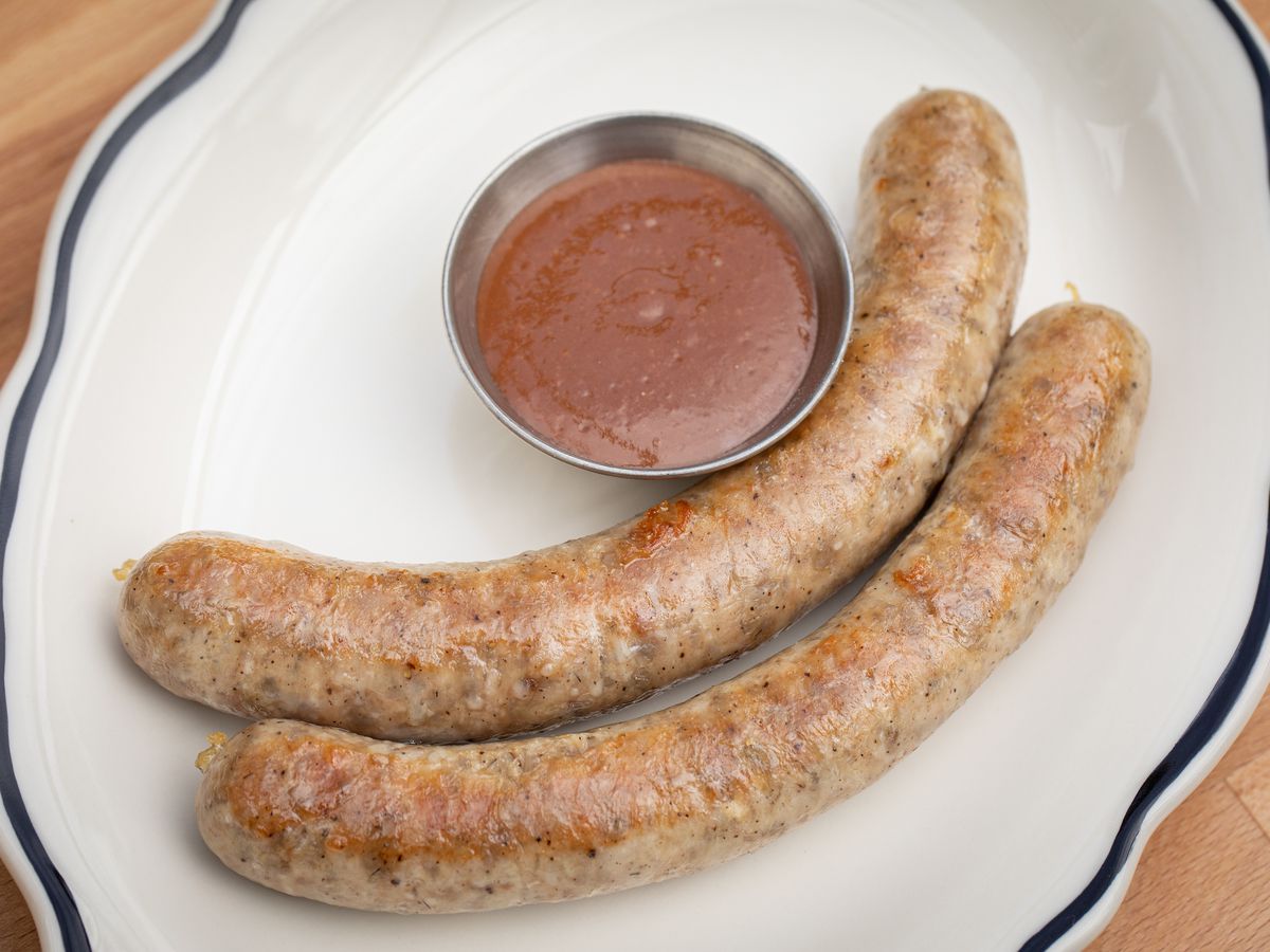 Two links of pork sausage with a side dish of red dipping sauce set together on a white plate