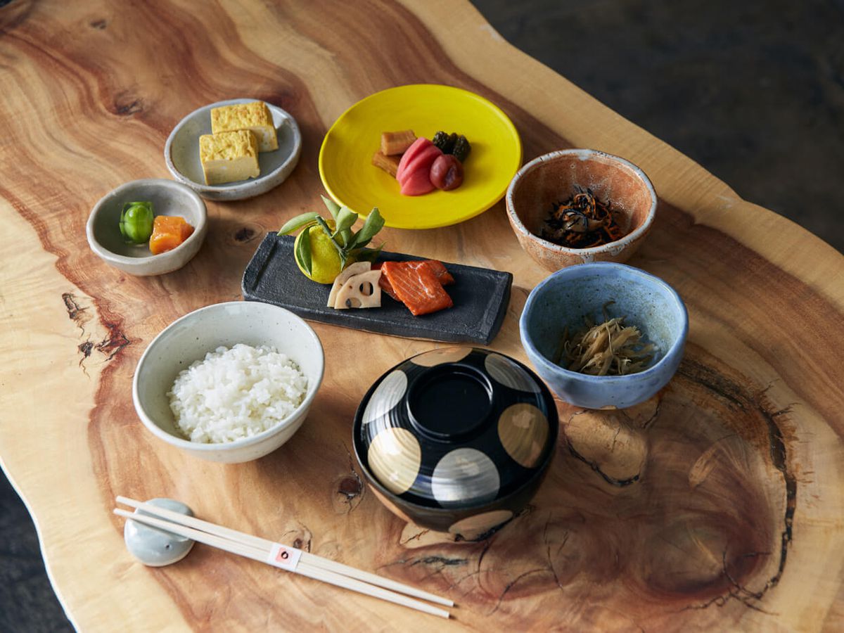 Japanese bowls hold fine foods during daylight hours atop a wooden table.