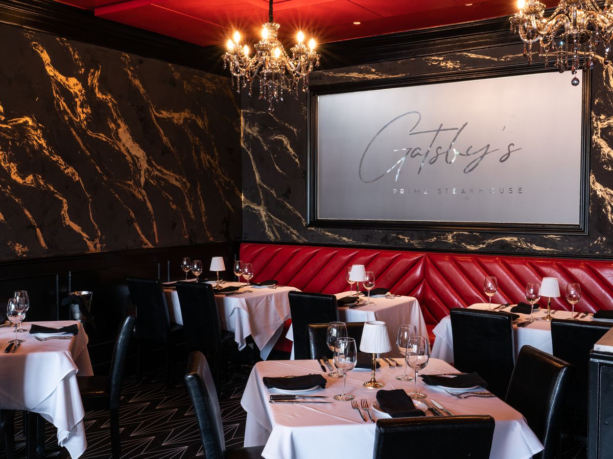Black and gold walls with red banquettes and a sign that reads Gatsby’s.