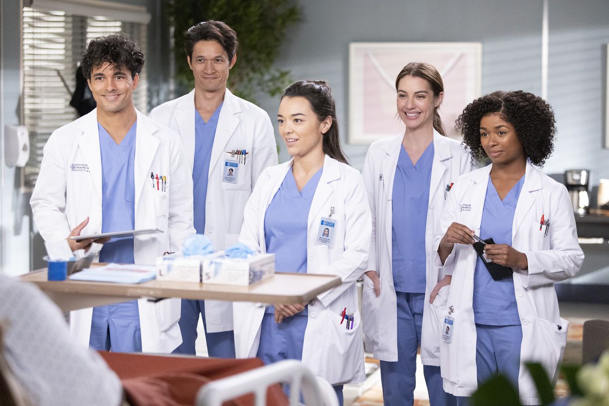 The new cast of interns on Grey’s Anatomy standing at the foot of a patient’s bed