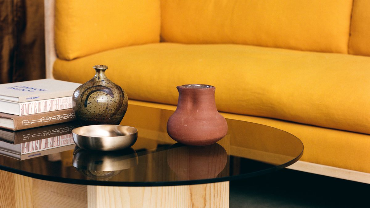 A yellow sofa, oval smoked glass coffee table with wood base, and terra cotta vessel.