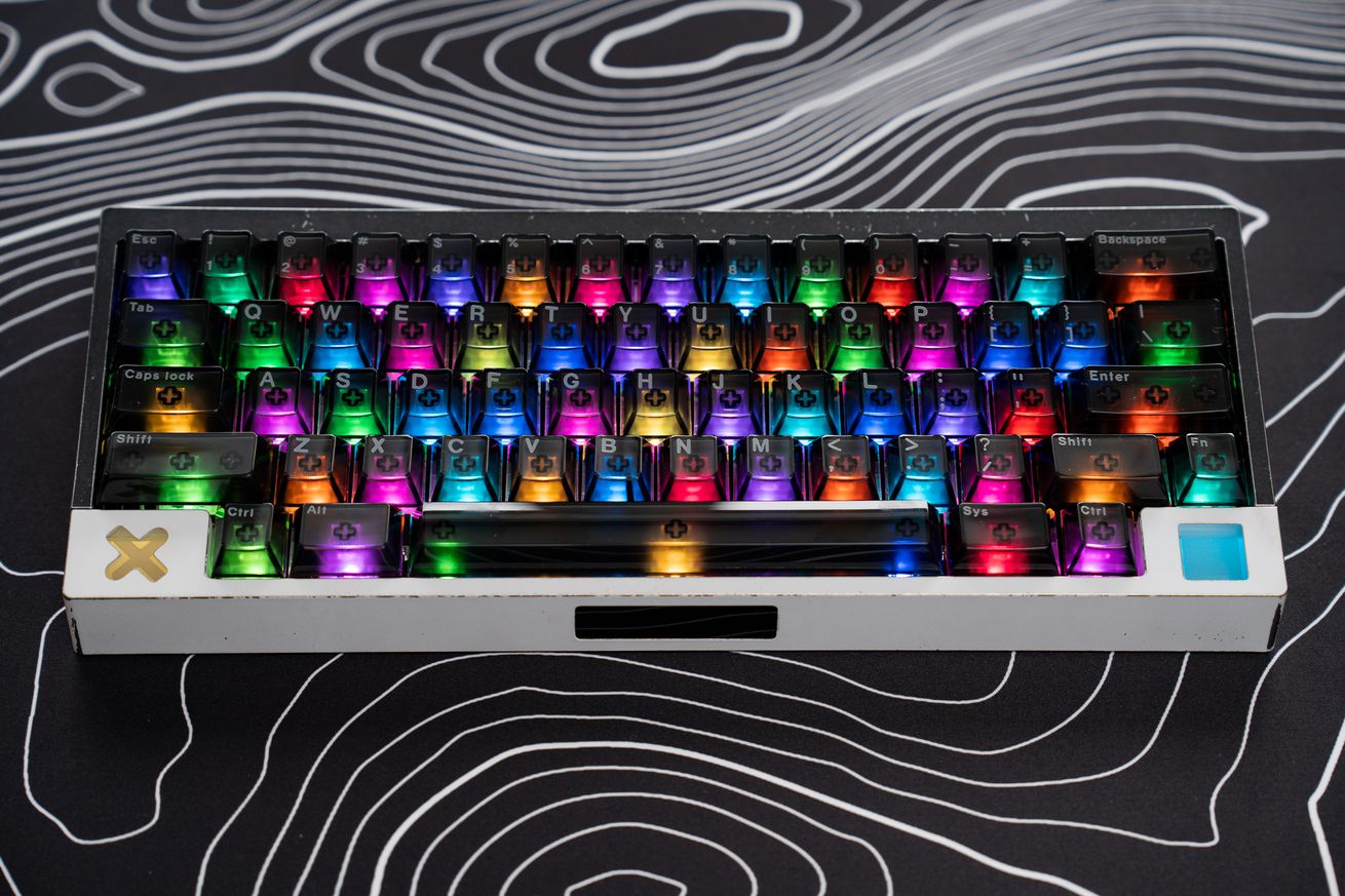 The Angry Miao Compact Touch keyboard in black and white “Mech Love” colorway with see-through smoked keycaps and predistressed metal case. The keyboard is sitting on a desk mat with its colorful RGB lighting on.