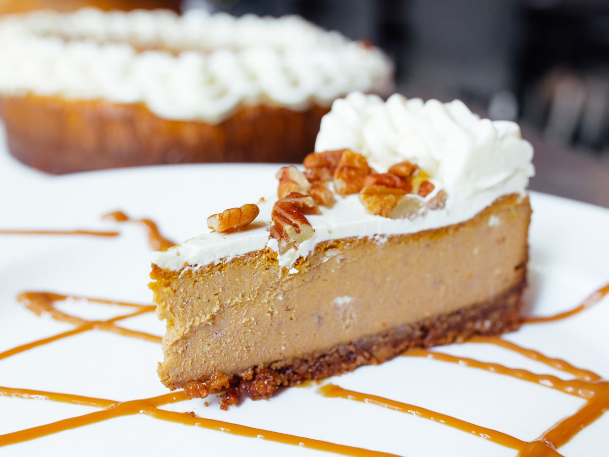 A slice of pumpkin cheesecake topped with whipped cream and pecans.