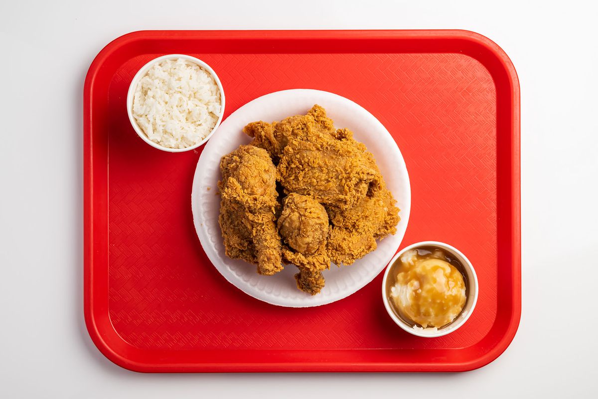 A red plastic tray holds a pile of Jollibee fried chicken and two bowls of mashed potatoes with gravy and rice.