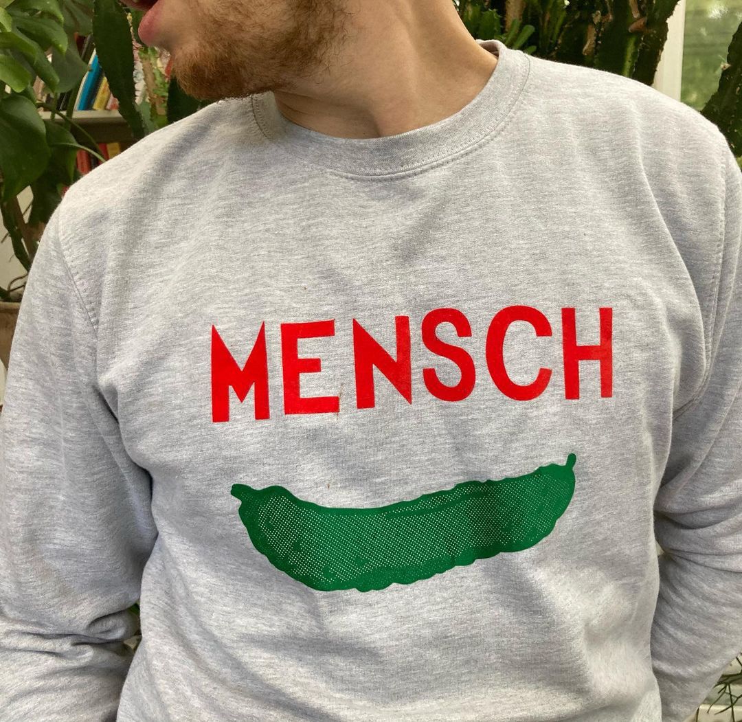 The best London restaurant merch to buy right now includes this sweater from Monty’s Deli with a green pickle design and red MENSCH lettering