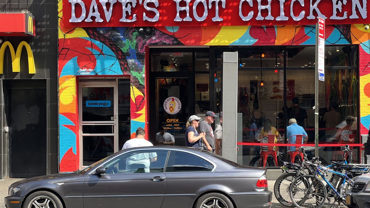The multi-colored exterior facade of Dave’s Hot chicken is shown with pedestrians walking by