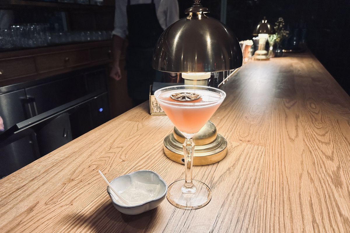 A pink drink in a martini glass next to a light. 