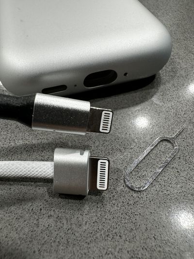 A picture of the Vision Pro battery connector removed from the battery, with a third-party lightning connector next to it and a SIM removal tool on the table by them.