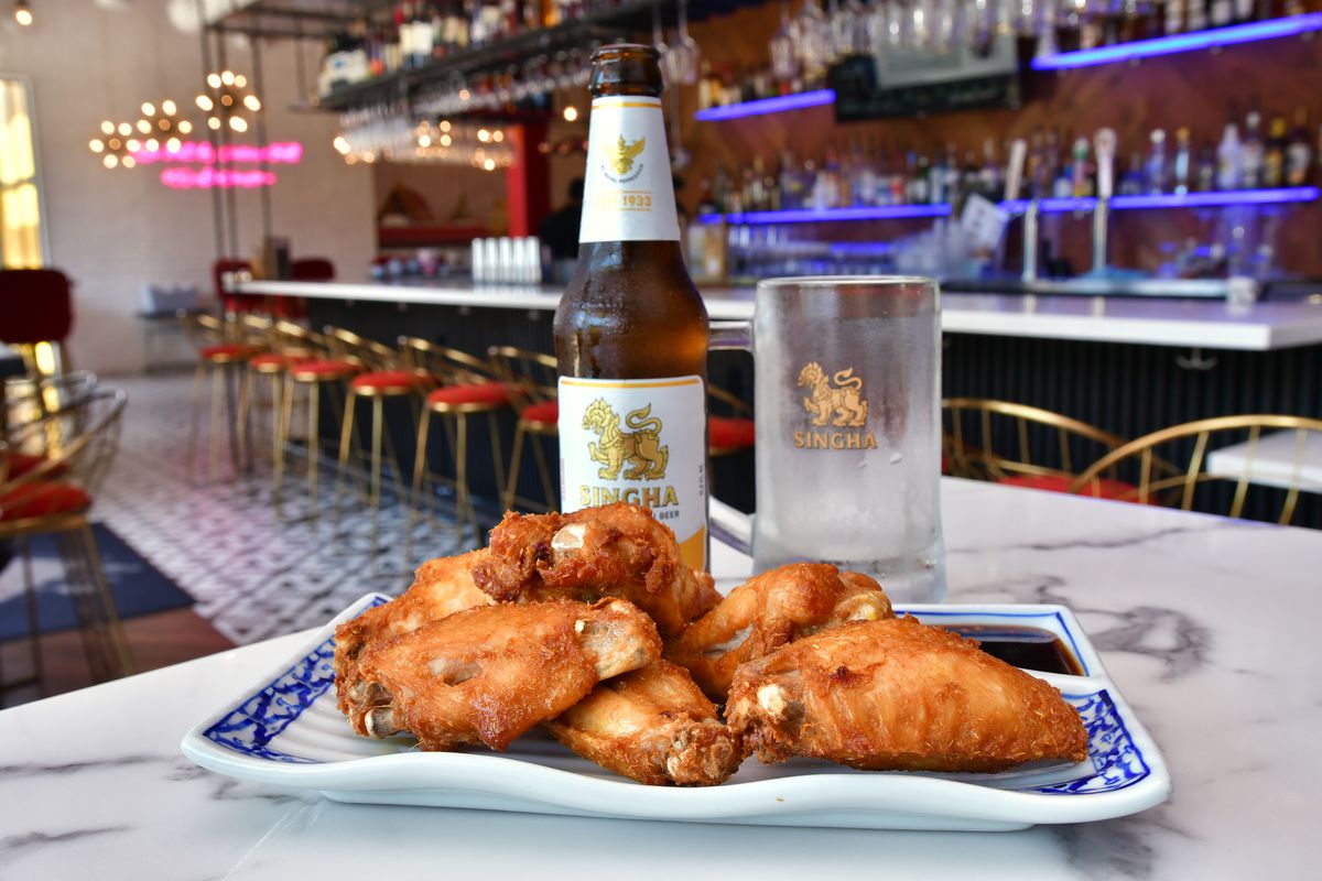 A plate of Kin Dee’s Kai Thod, or Thai fried chicken wings, with a Singha bottle of beer and frosted glass, with views of its bar.