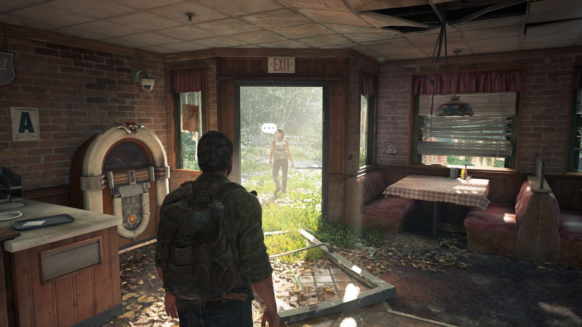 Joel in an abandoned pizzeria as Tess walks out with a speech bubble beside her head in The Last of Us Part 1