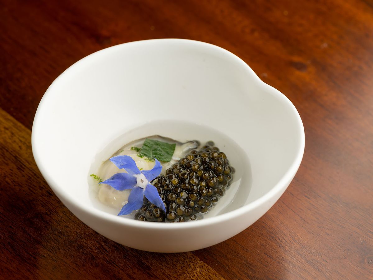 Oyster and caviar with a blue petal in a white bowl.