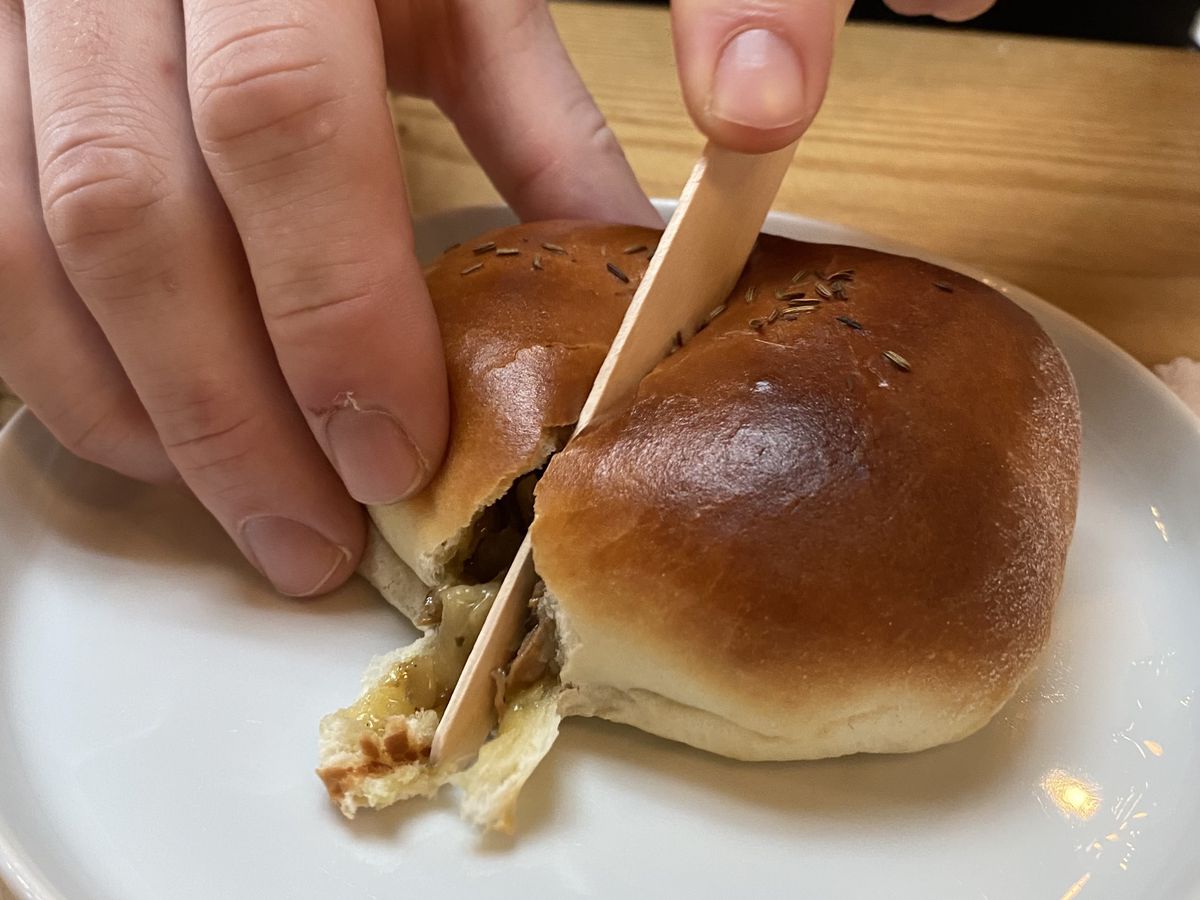 A hand holding a knife slices into a perfectly brown-on-top bun, revealing a beefy filling.