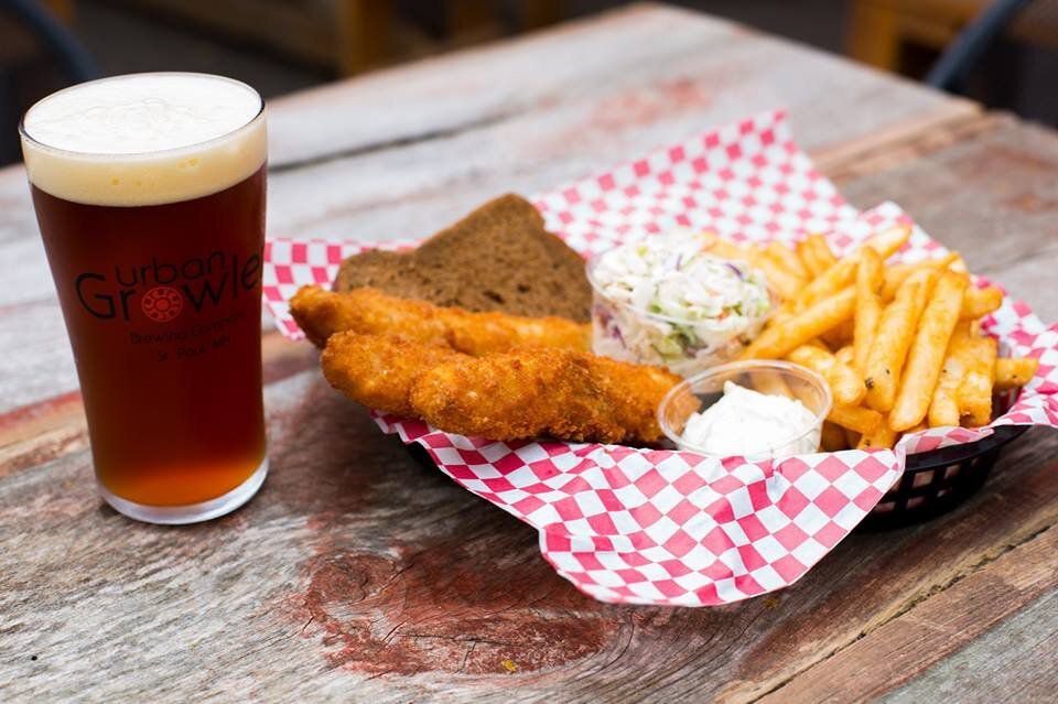 Fried fish and french fries with coleslaw on red and white checked paper in a basket next to a pint of beer. 