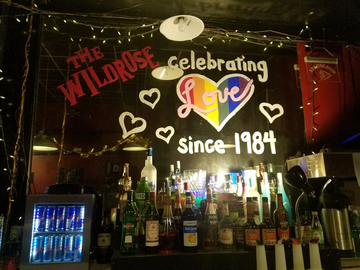 A sign behind a bar reading “The Wildrose, celebrating love since 1984.”