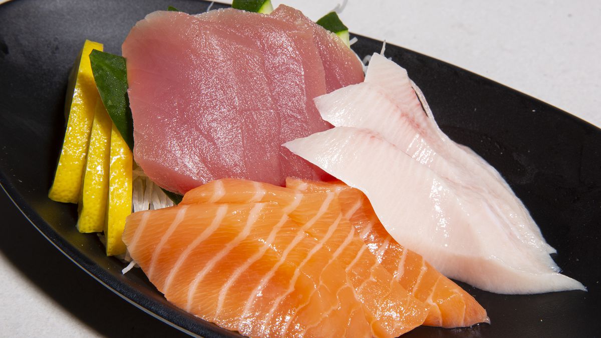 Thick slices of tuna, salmon, and yellowtail sashimi in a black bowl.