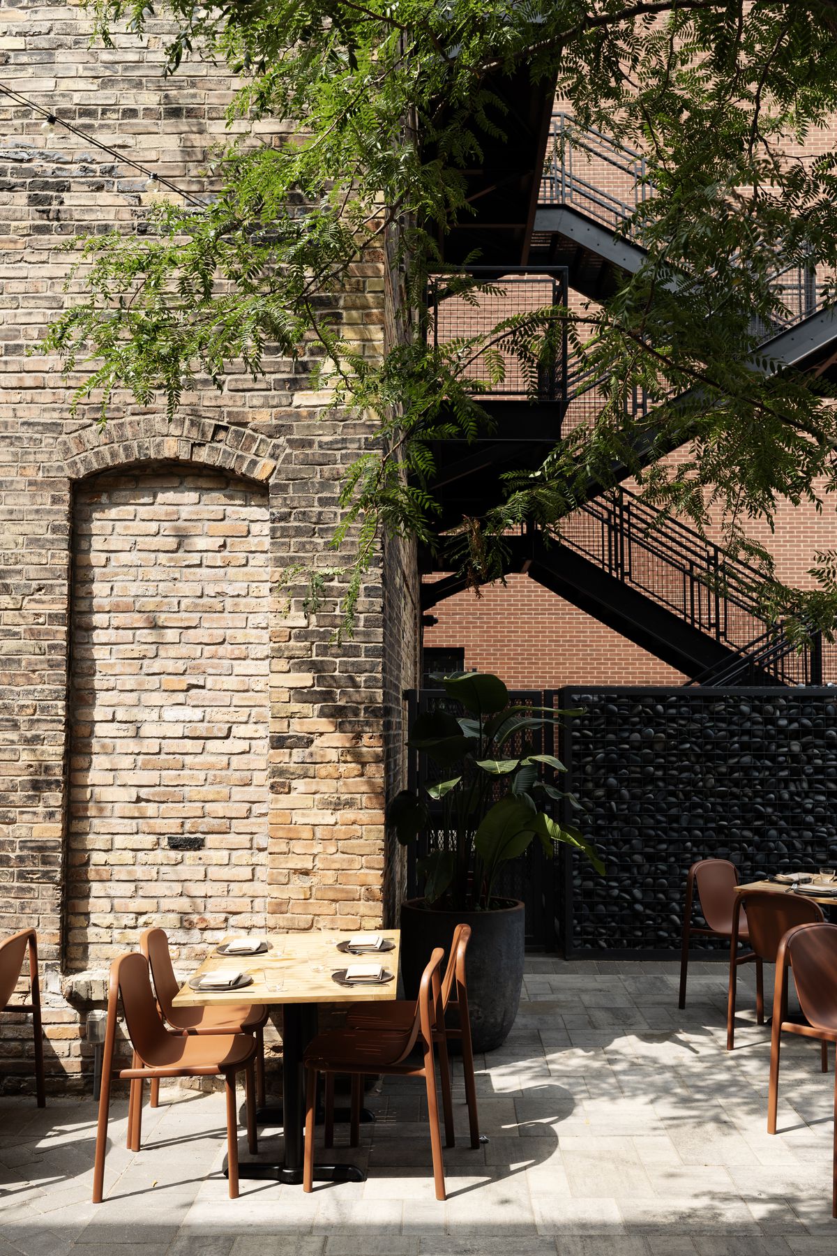 A table with four chairs outside a brick building in an alleyway patio space. 