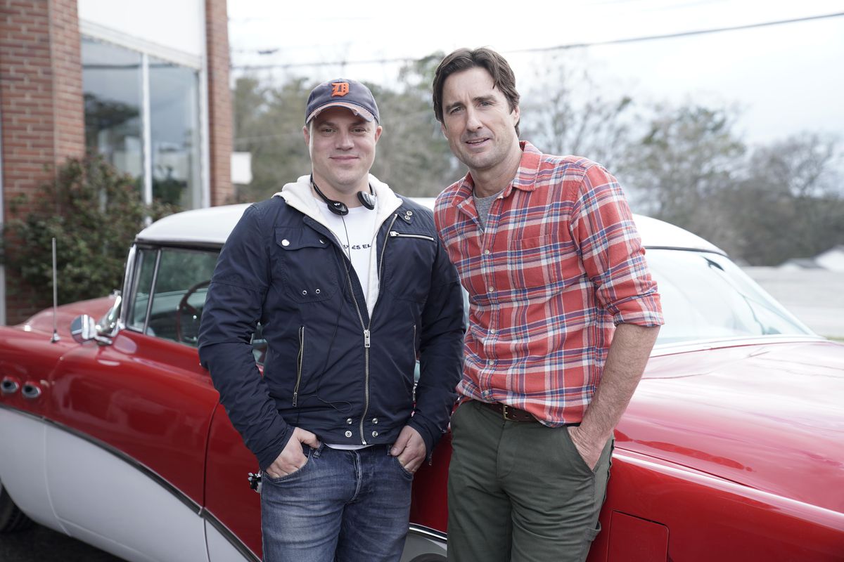 Geoff Johns and Luke Wilson on the set of Stargirl. They’re standing in front of a red and white restored classic convertible, the show’s version of the Star Rocket Racer.