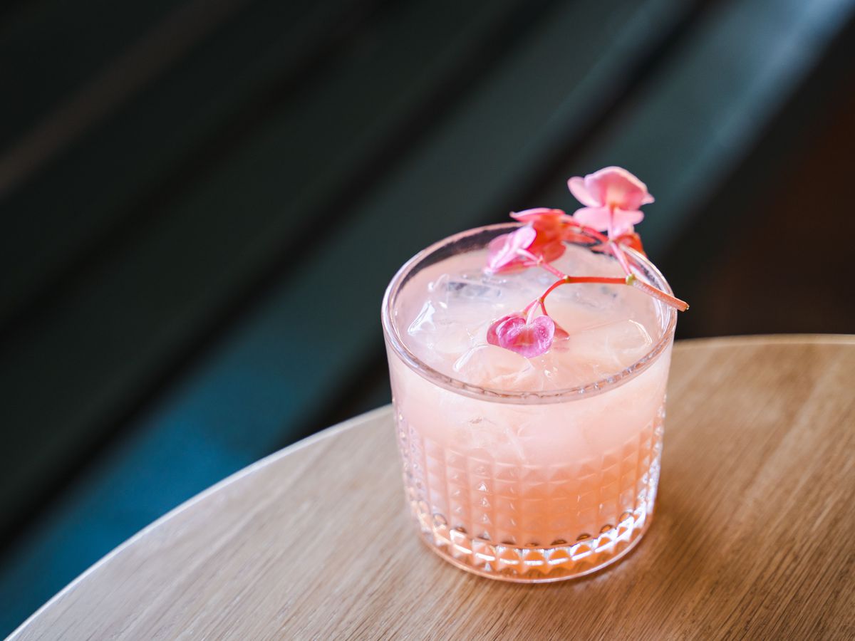 Pink cocktail with flowers against dark background 