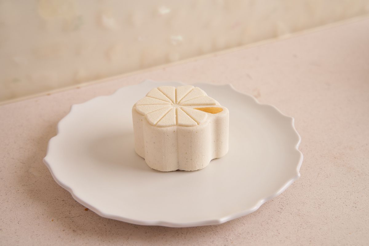 An off-white cake that looks like a paperweight sits on a white plate