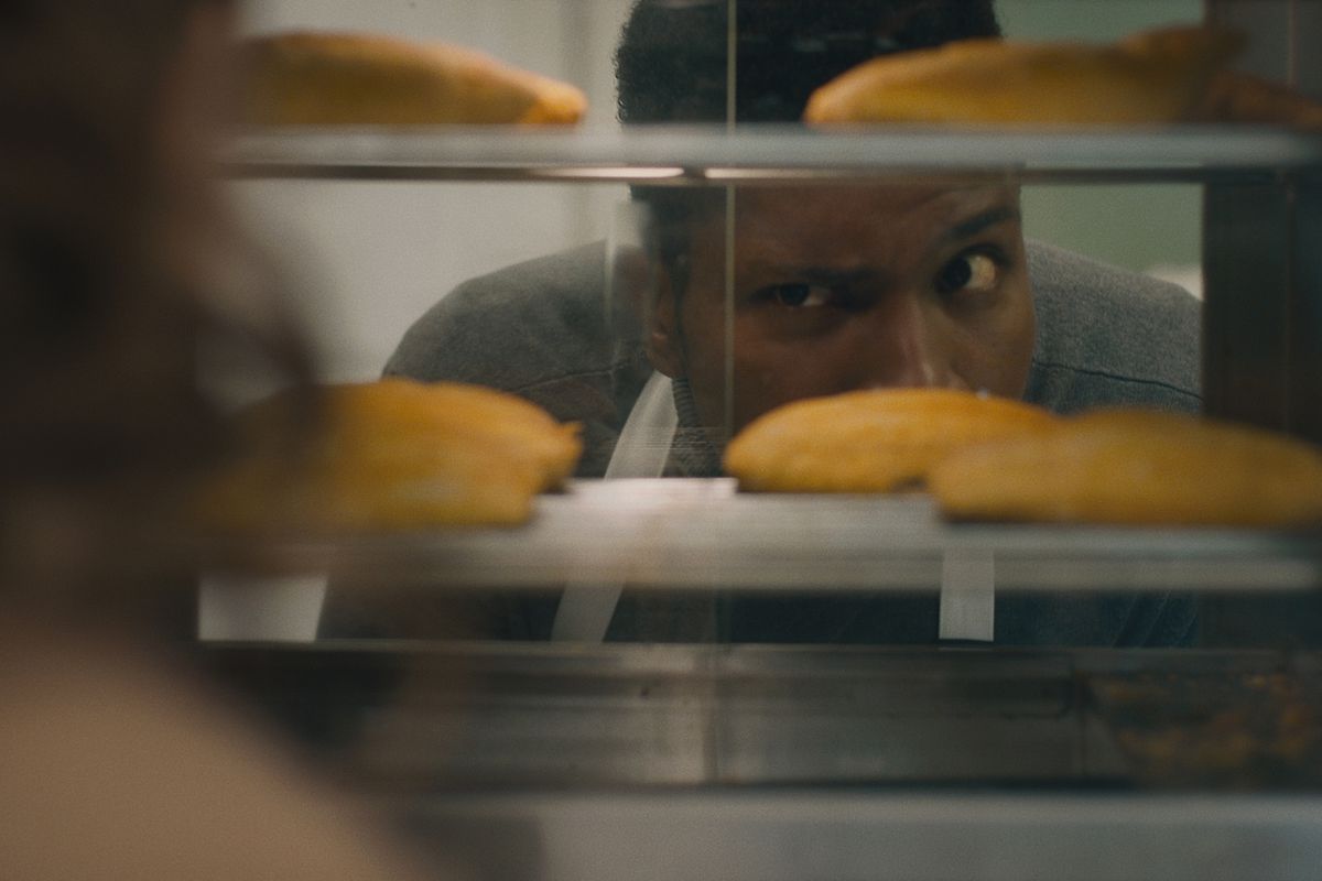 A man peers through a pastry case at a row of Jamaican beef patties.