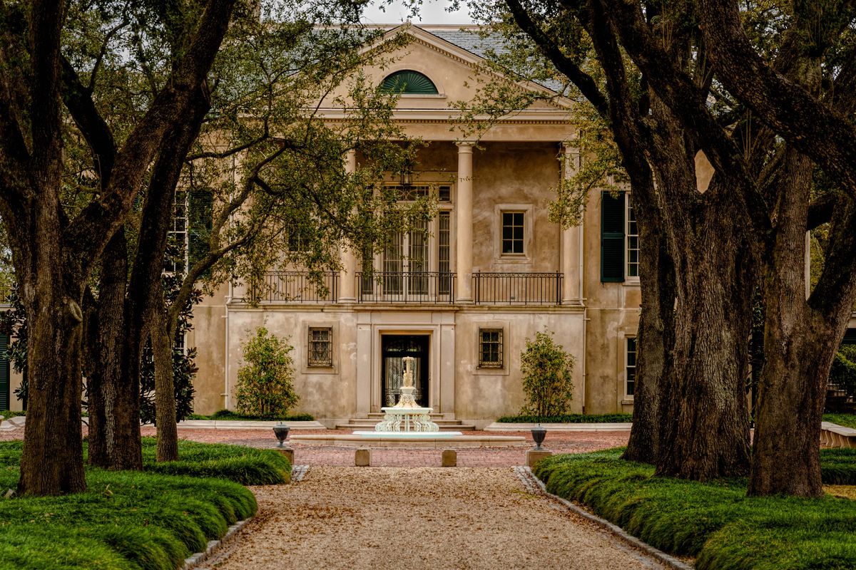 A large historic home in New Orleans that has a path leading up to its entrance through trees. 