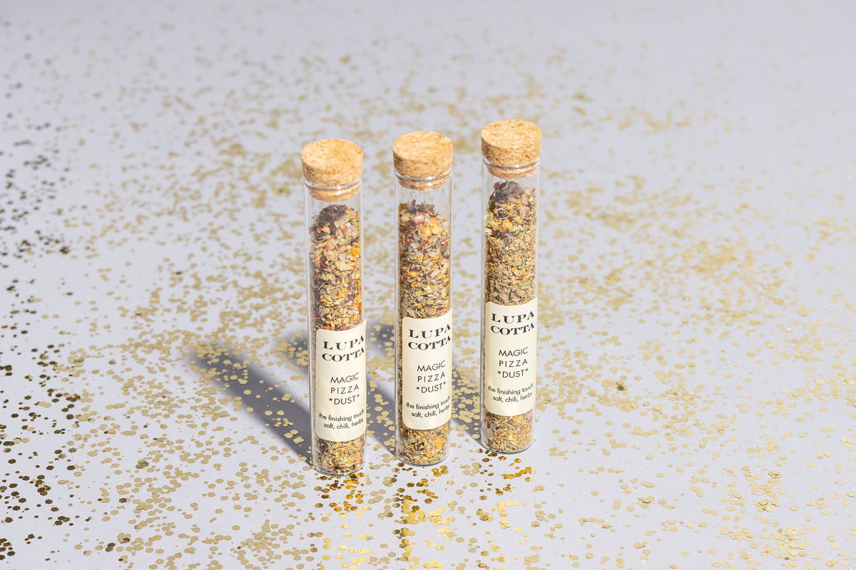 Three vials of a pizza spice blend from Lupa Cotta containing oregano and sea salt on a background with gold confetti.