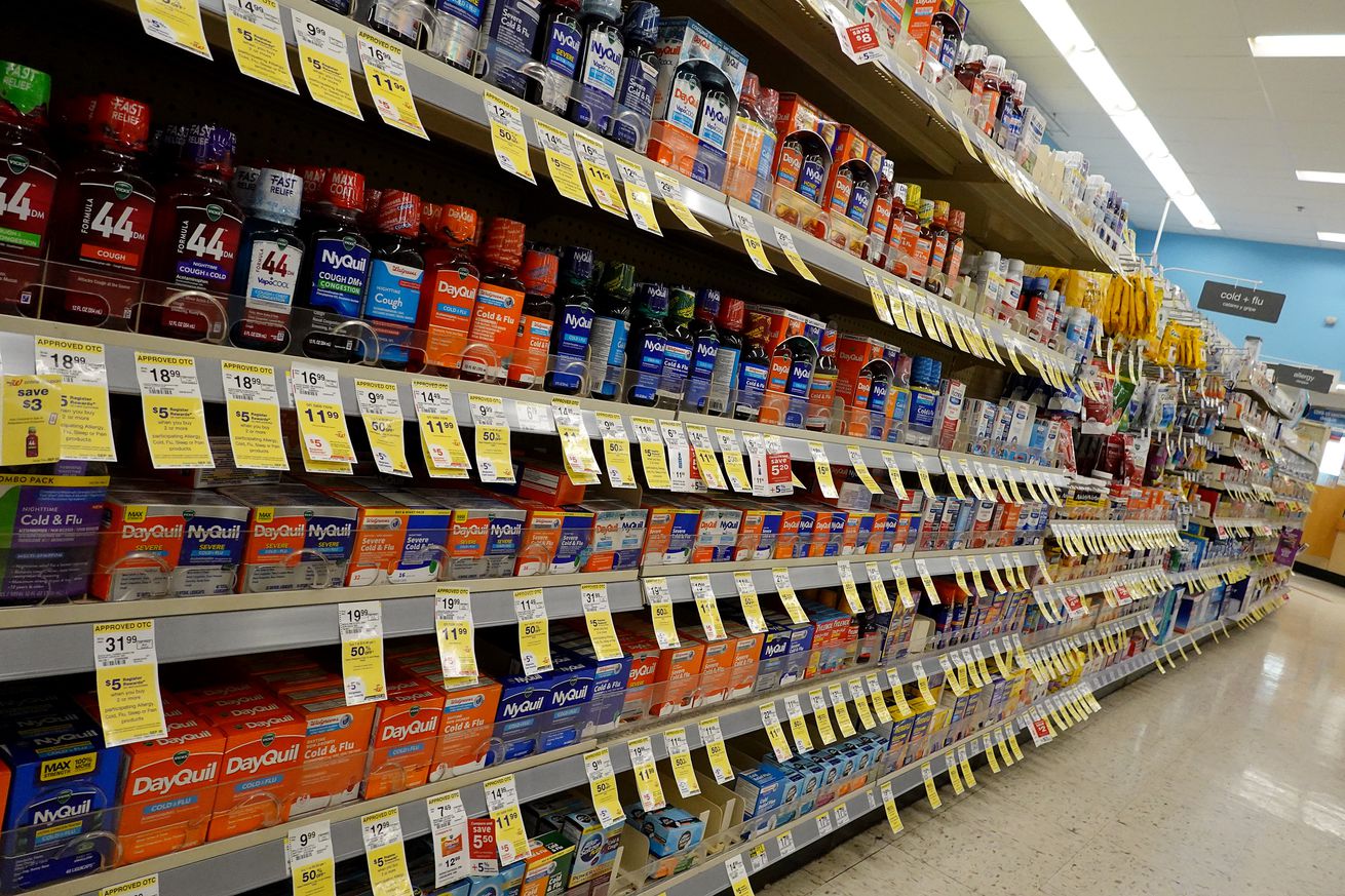A picture of shelves containing cold medications on a store shelf, with price tags hanging on the bottom of the shelves.
