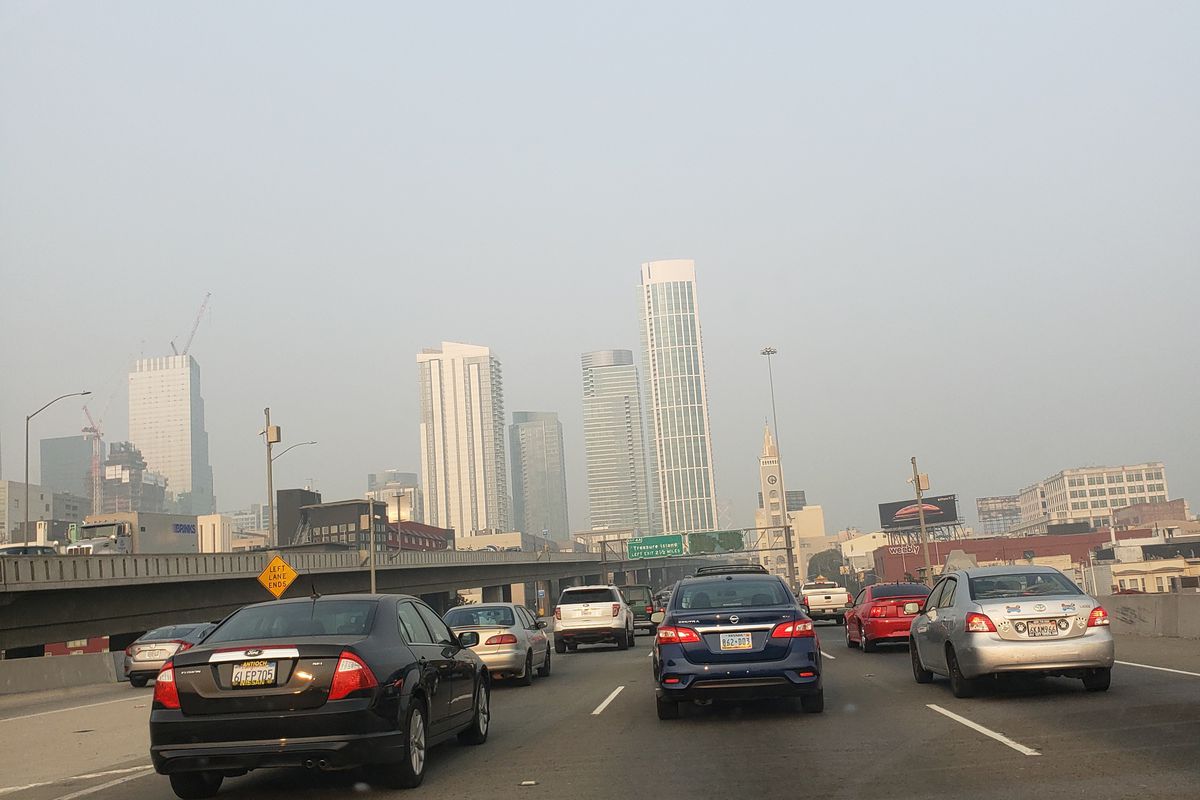 Gray smoke hovering over a series of high-rise buildings, with cars on the freeway below.