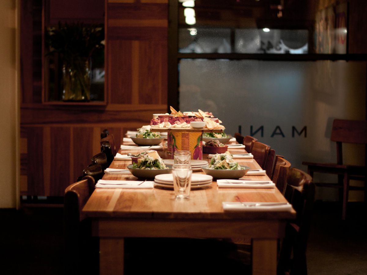 A dimly lit room with a large butcher block table set up with salads and a cheese plate on a pedestal.