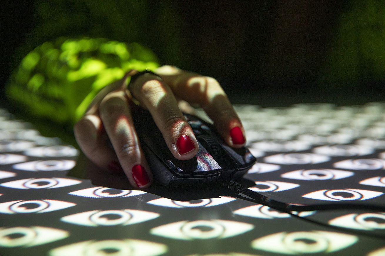 Photograph of a hand wearing red nail varnish holding a mouse with a projection overlay of stylized eyes