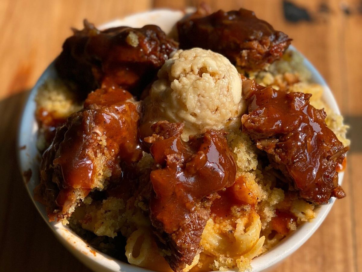 A bowl of vegan mac and cheese and fried chicken topped with sauce and butter. 