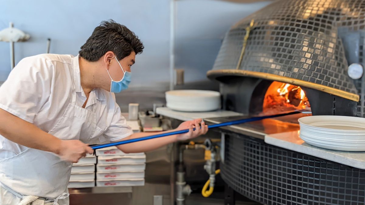 William Joo of Pizzeria Sei puts a pizza into a woodfired oven.