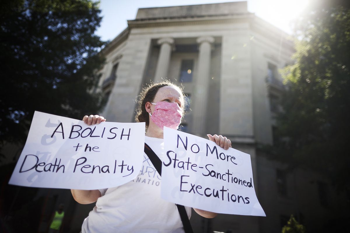 A person standing in front of the Justice Department building holds signs that read “Abolish the death penalty” and “No more state-sanctioned executions.”