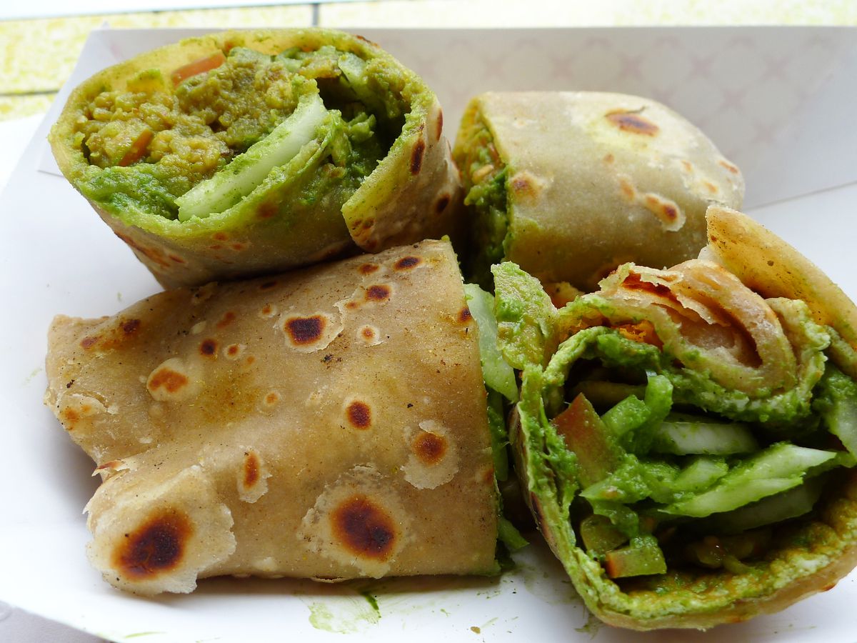 A pair or flatbread rolls, each cut in two and propped up, filled with green vegetables.