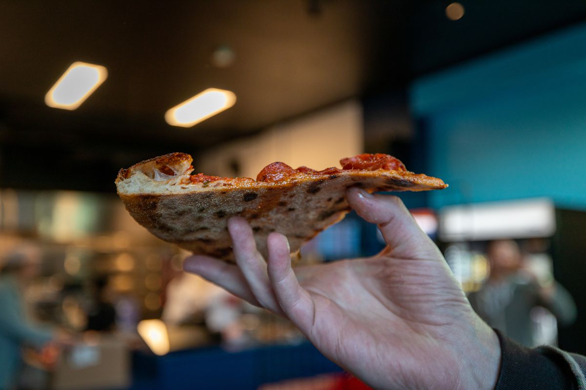 A hand holding up a thin slice of pizza.