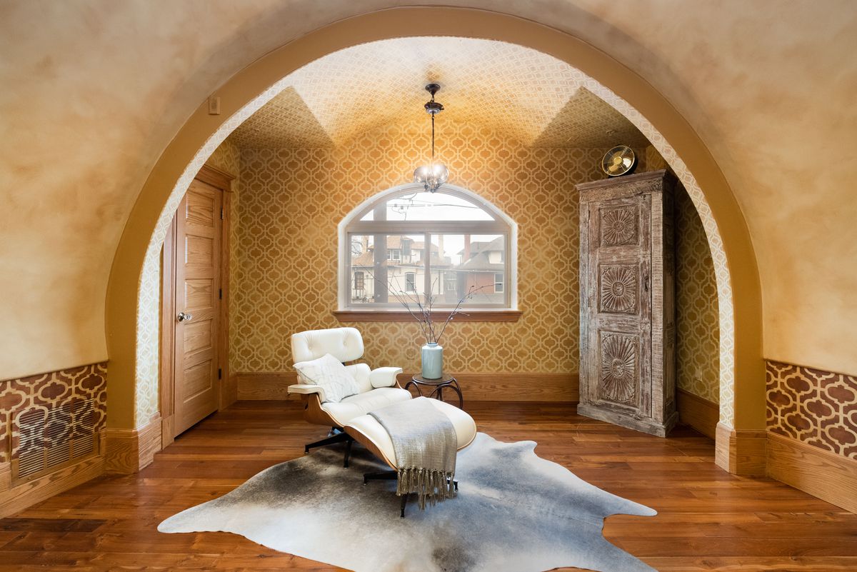 An Eames-style chair sits on an animal rug underneath a second-story arch. 