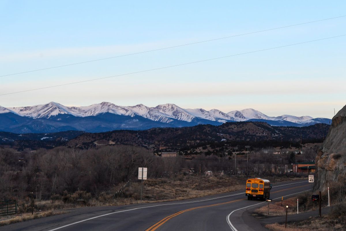 A school bus from the Primero district drives down a highway with the Sangre de Cristo mountains in the background.