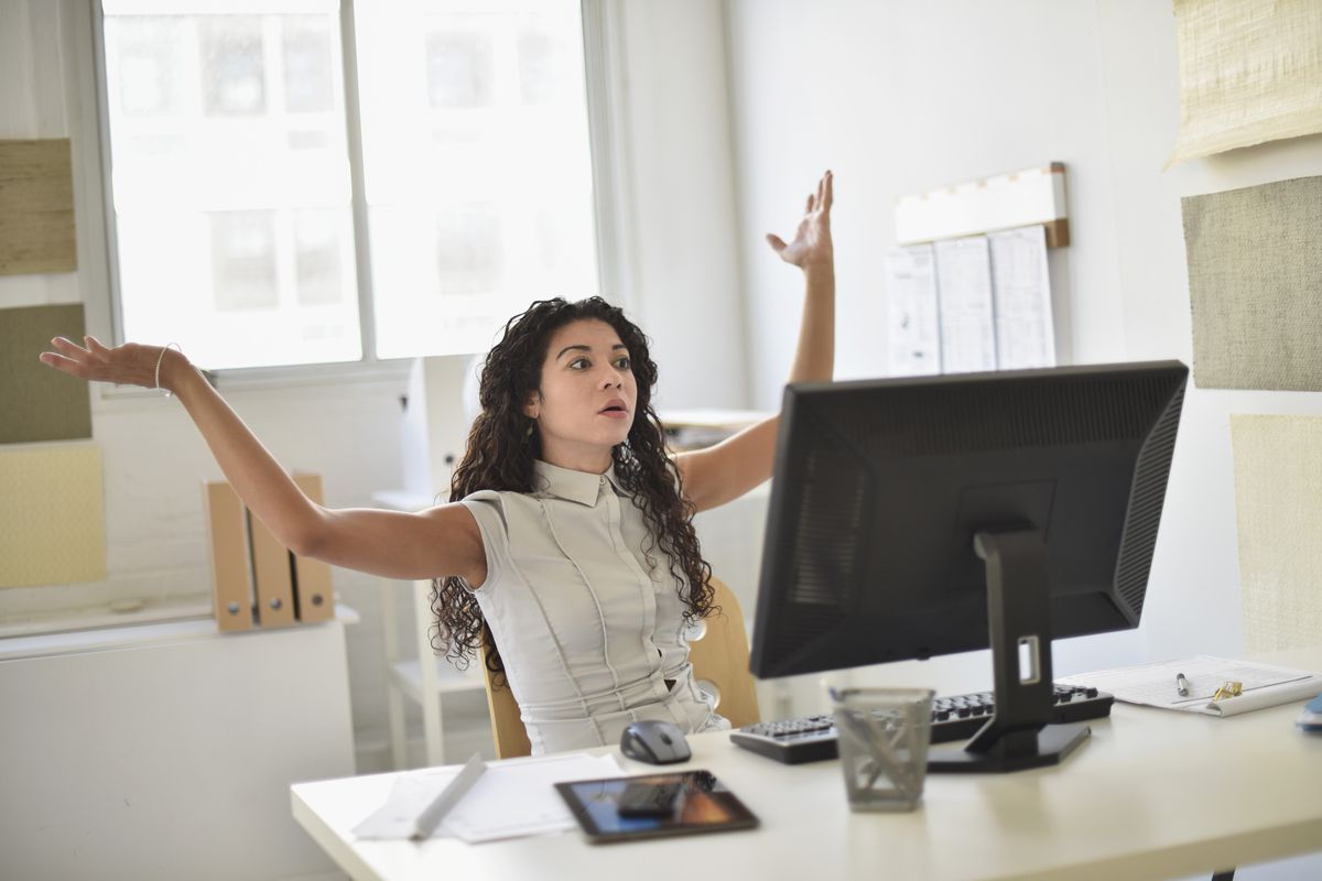 A woman throws her hands up in front of a computer.