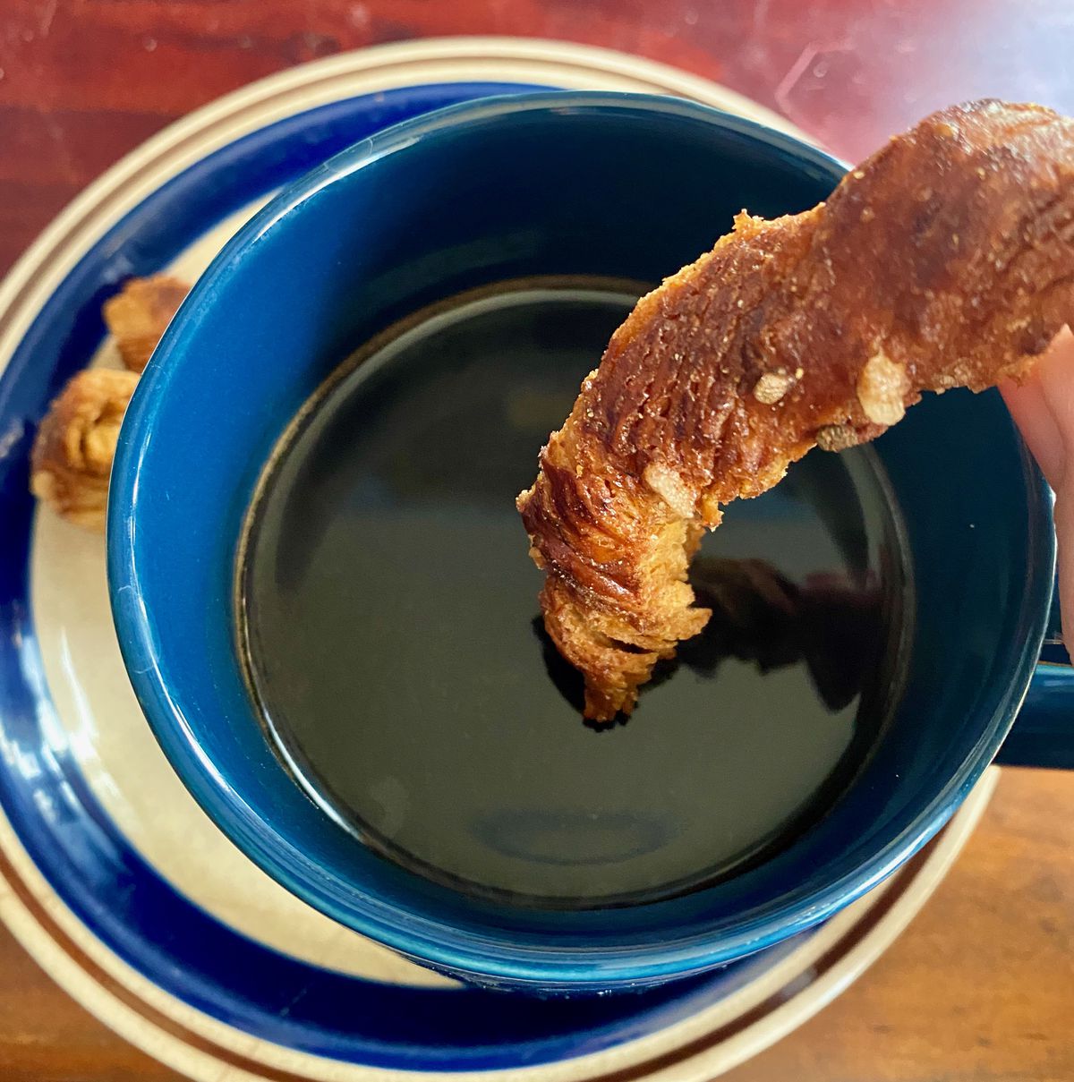 A brown pastry rests on top of the surface of a dark liquid inside a blue mug