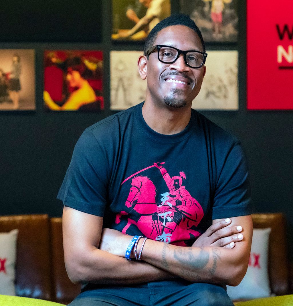 Yasuke creator and director LeSean Thomas sits smiling in a graphic t-shirt with his arms crossed.