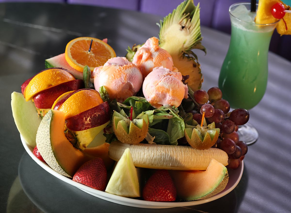 A platter of peeled fruits and a blue cocktail.