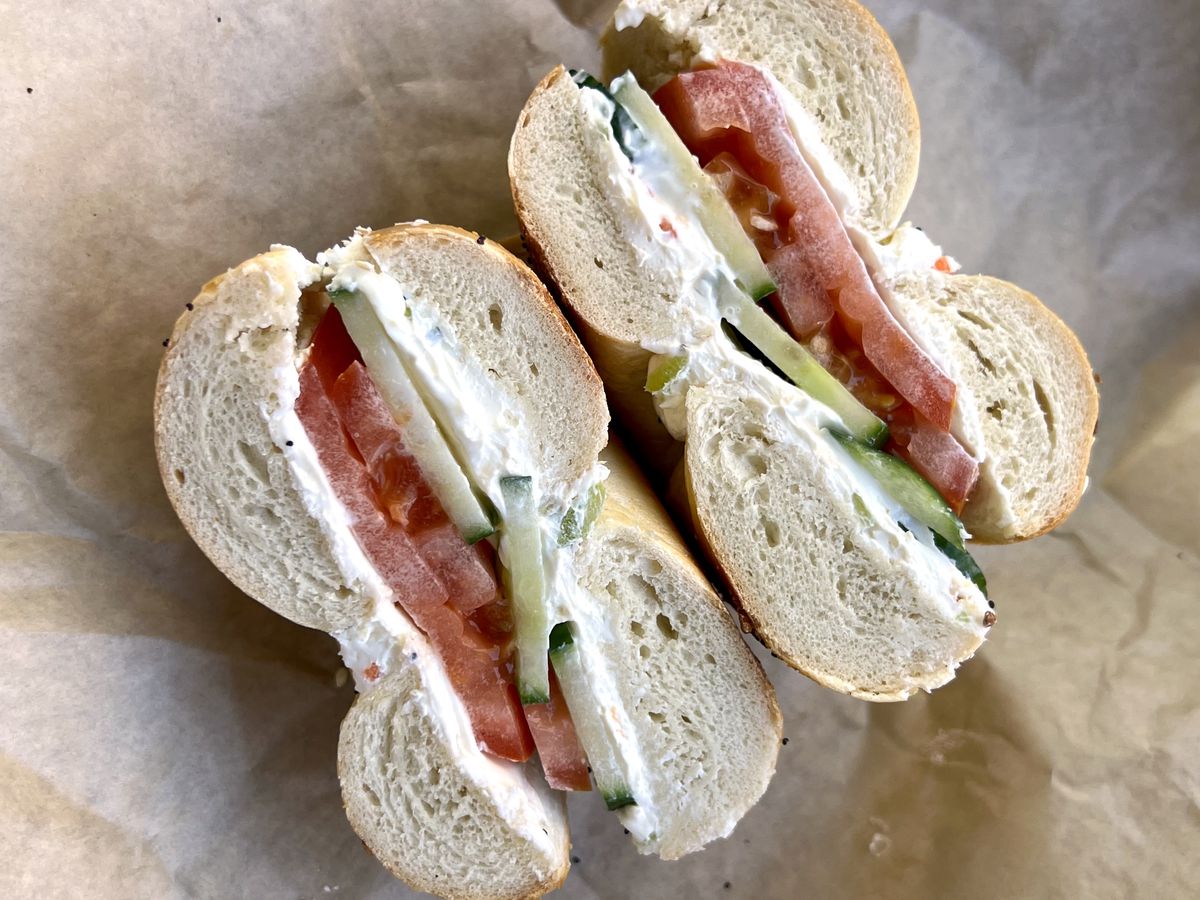 A bagel sandwich on parchment paper with tomatoes, cucumbers, and cream cheese from East Coast Bagels. 