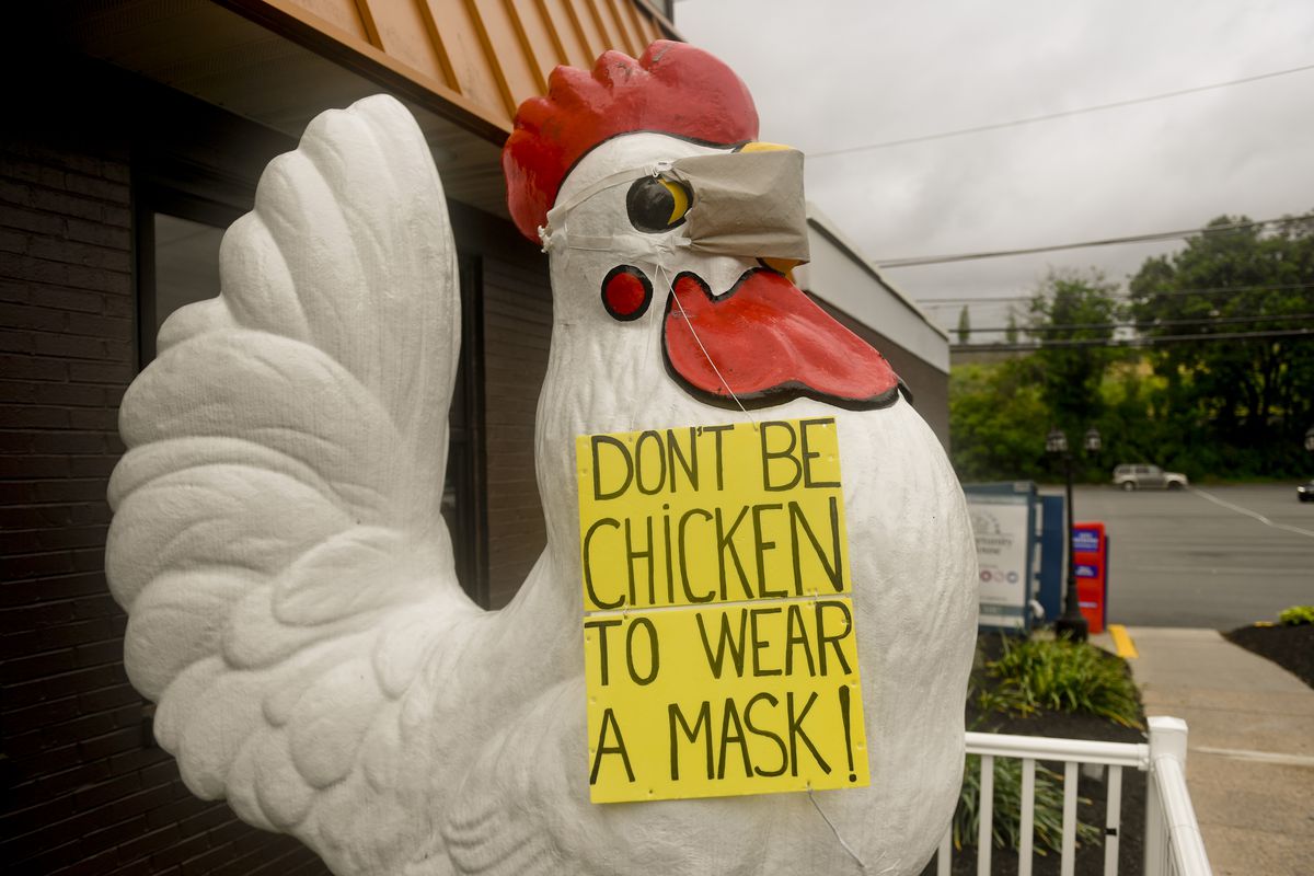A giant chicken statue outside a restaurant wears a face mask and a sign reading, “Don’t be chicken to wear a mask!”