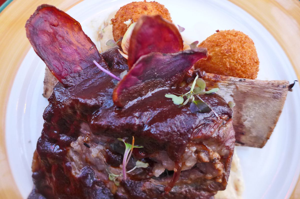 A bare rib sticks out of a lake of brown sauce with deep fried potatoes on the side of the plate.