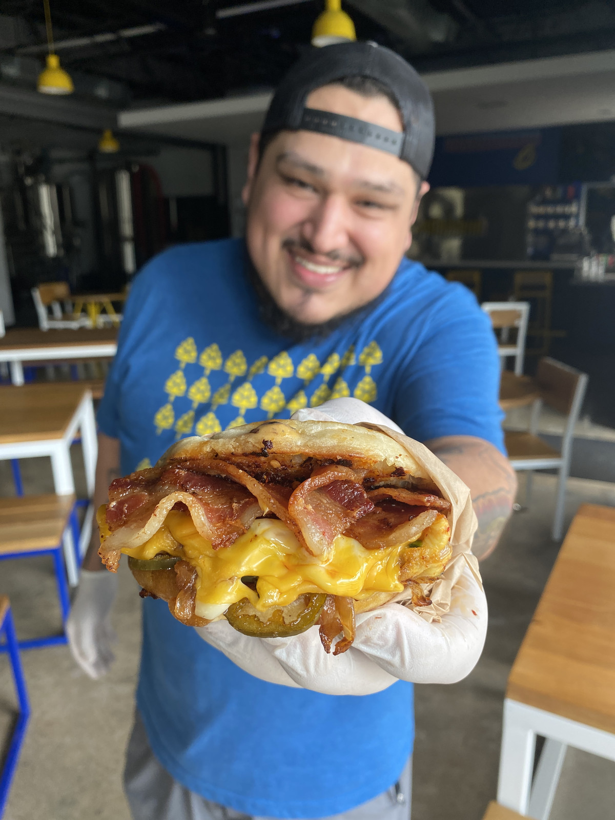 Chef Daniel Leal holding a breakfast sandwich loaded with cheesy eggs and a slab of bacon.