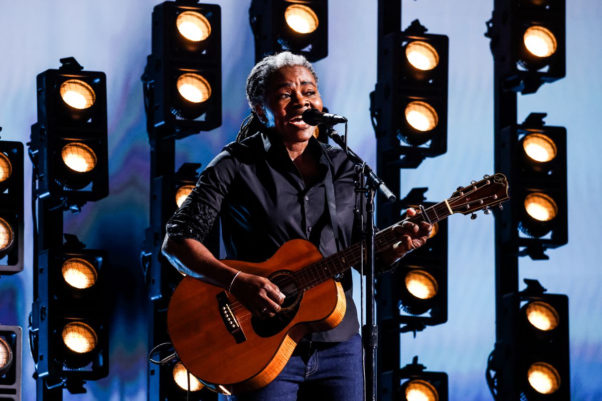 Tracy Chapman, a Black woman singing into a microphone and holding a guitar, performs onstage with stage lights behind her during the 66th Grammy Awards on February 4, 2024, in Los Angeles.
