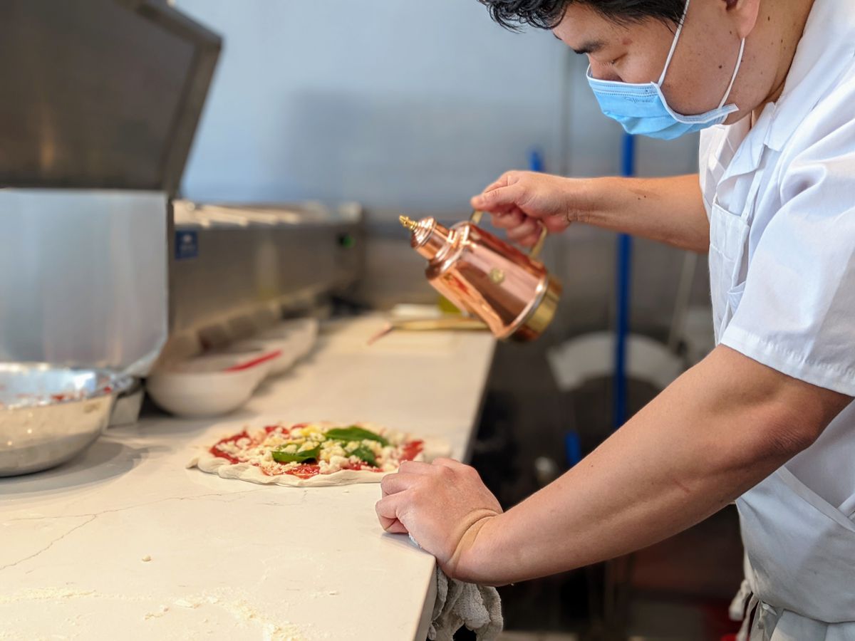 William Joo pours olive oil on a pizza before baking at Pizzeria Sei using a copper kettle.