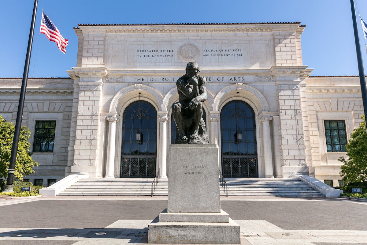 Front entrance of the Detroit Institute of Arts. There’s a black statue in front of the double marble arched entrance. 