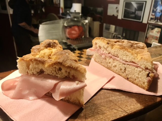 Two paninis on a cutting board overflowing with slices of. mortadella