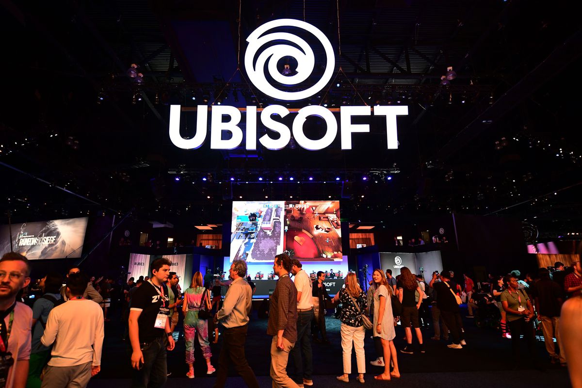 people standing below a Ubisoft logo at the company’s E3 2019 booth